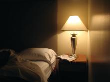 A lit lamp and a book on a bedside table